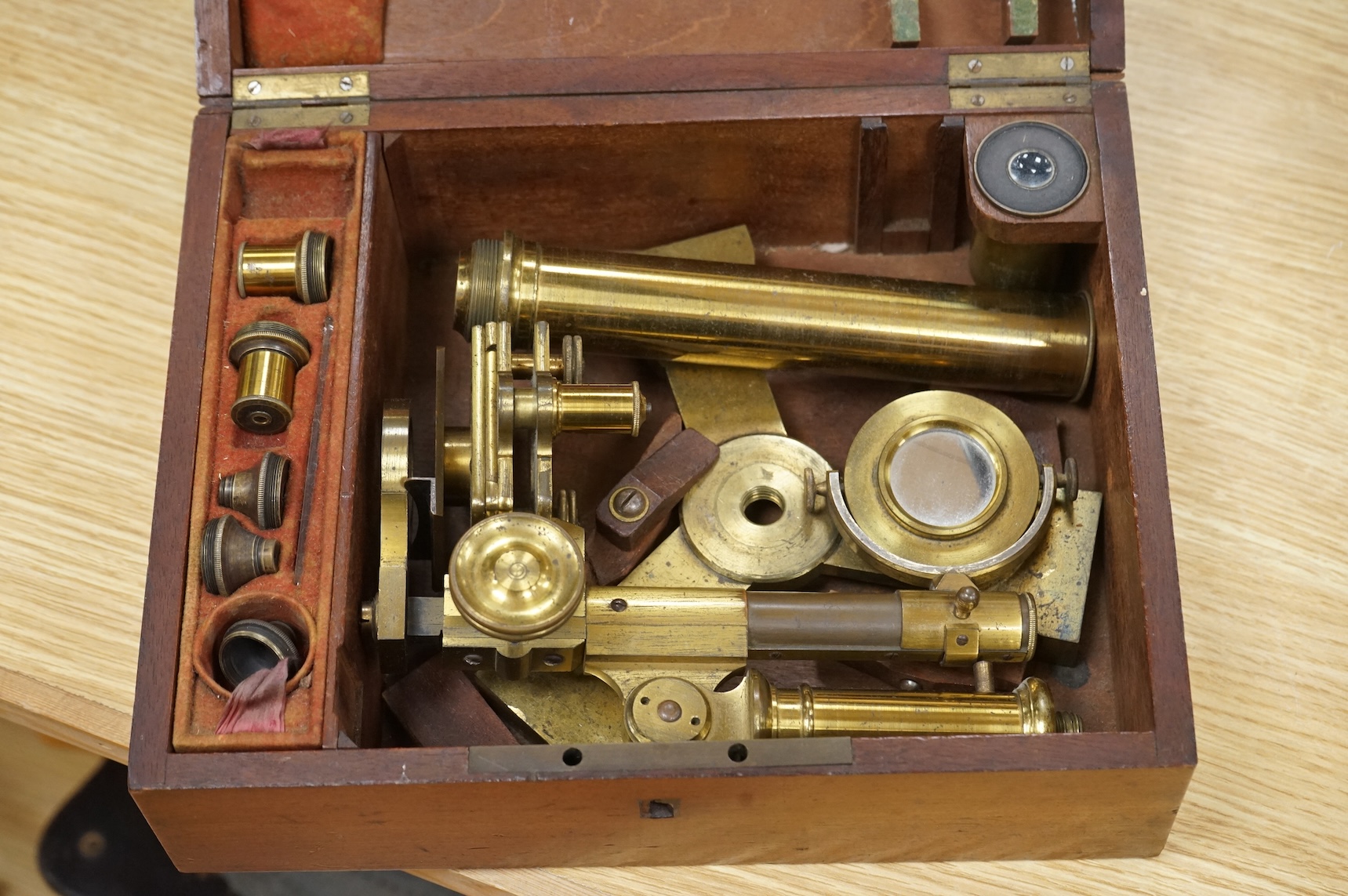 A mahogany cased 19th century brass field microscope, the body separates into sections, in a fitted case together with a selection of alternative lenses and other accessories, the microscope is unsigned, when closed the